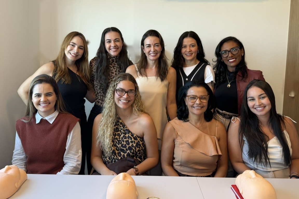 Turma do curso sorrindo com a Dra. Mariana Negreiros, com os manequins na mesa